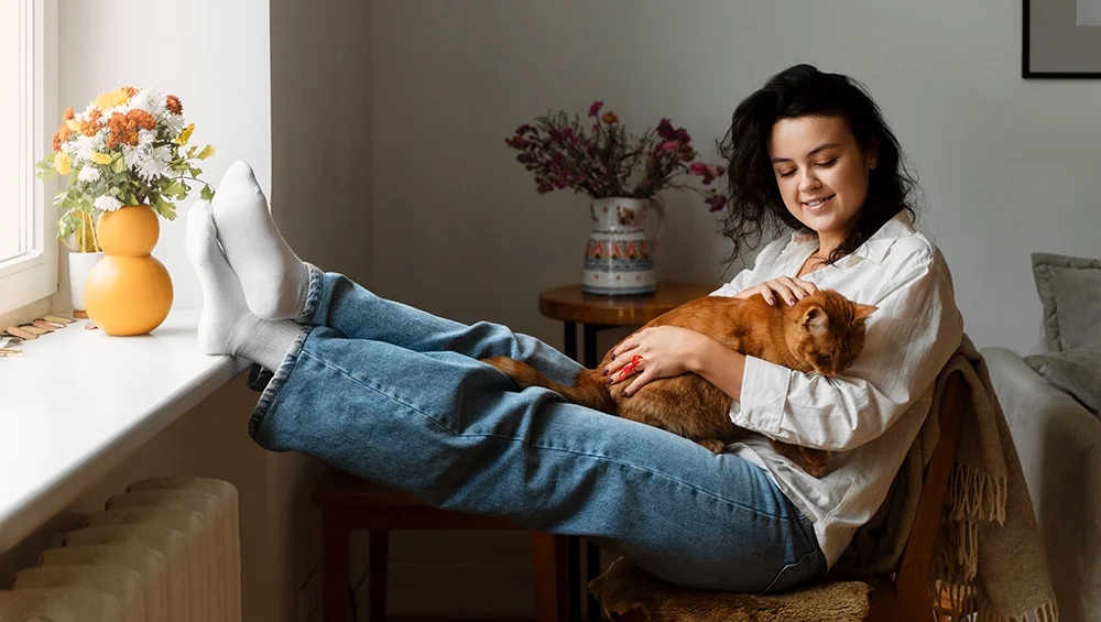 A young woman puts her feet up at home with her happy orange cat in her lap